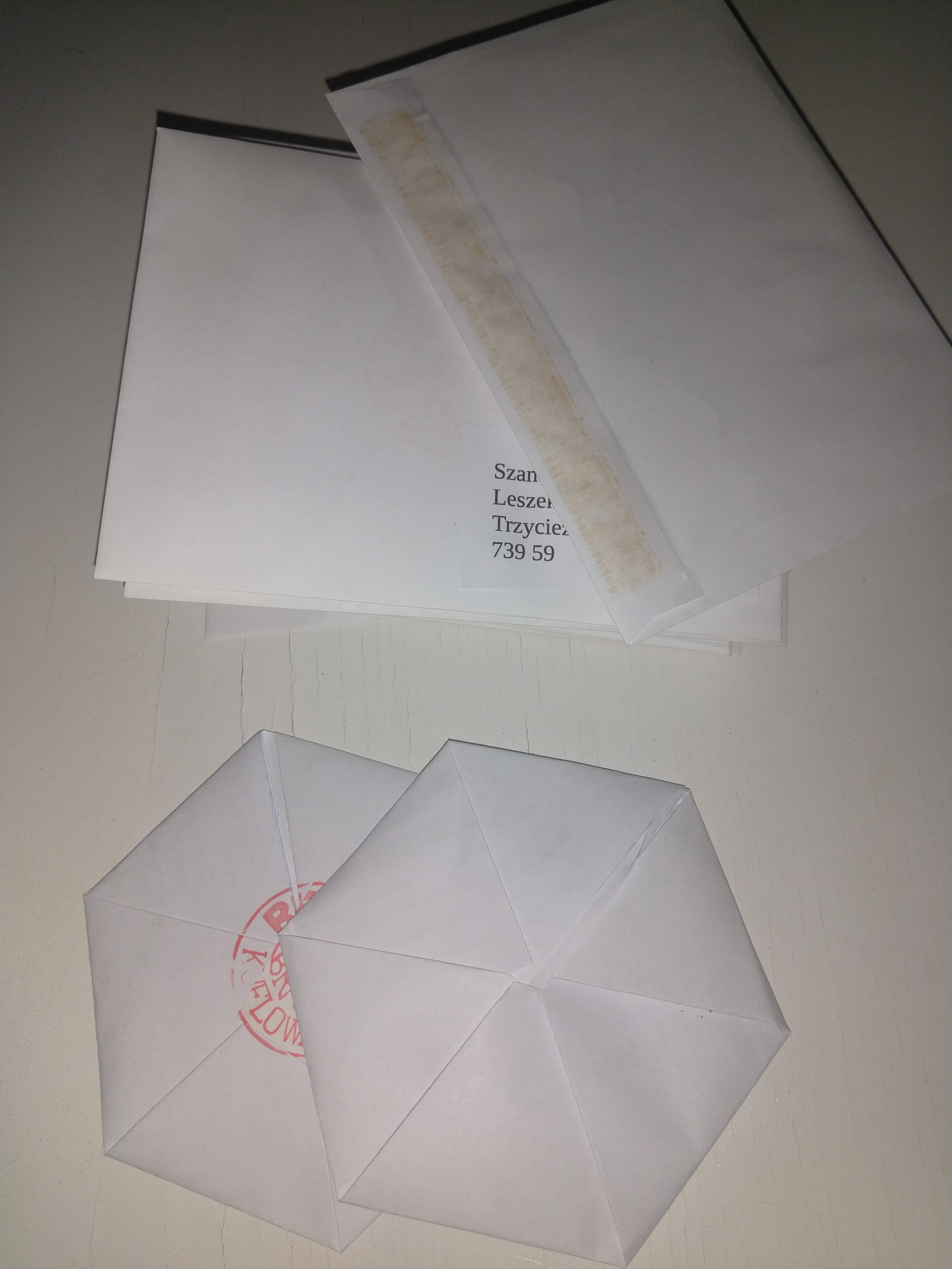 Koperty z adresami. Poniżej dwie kartki poskładane metodą origami w kształt sześciokąta. Na jednym sześciokącie widoczny stempel pieczętujący.